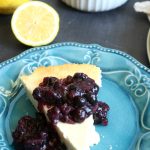 cheesecake on blue plate with blueberry compote on top