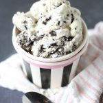 A cup filled with cookies and cream ice cream on a towel with a spoon nearby.
