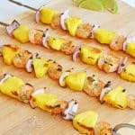 Grilled shrimp skewers with pineapple chunks and red onion on a wooden board.