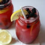 Two mason jars filled with refreshing blackberry lemonade, garnished with blackberries and a lemon slice. Each jar has a straw, and a lemon half sits nearby—perfect inspiration for your next blackberry lemonade recipe.