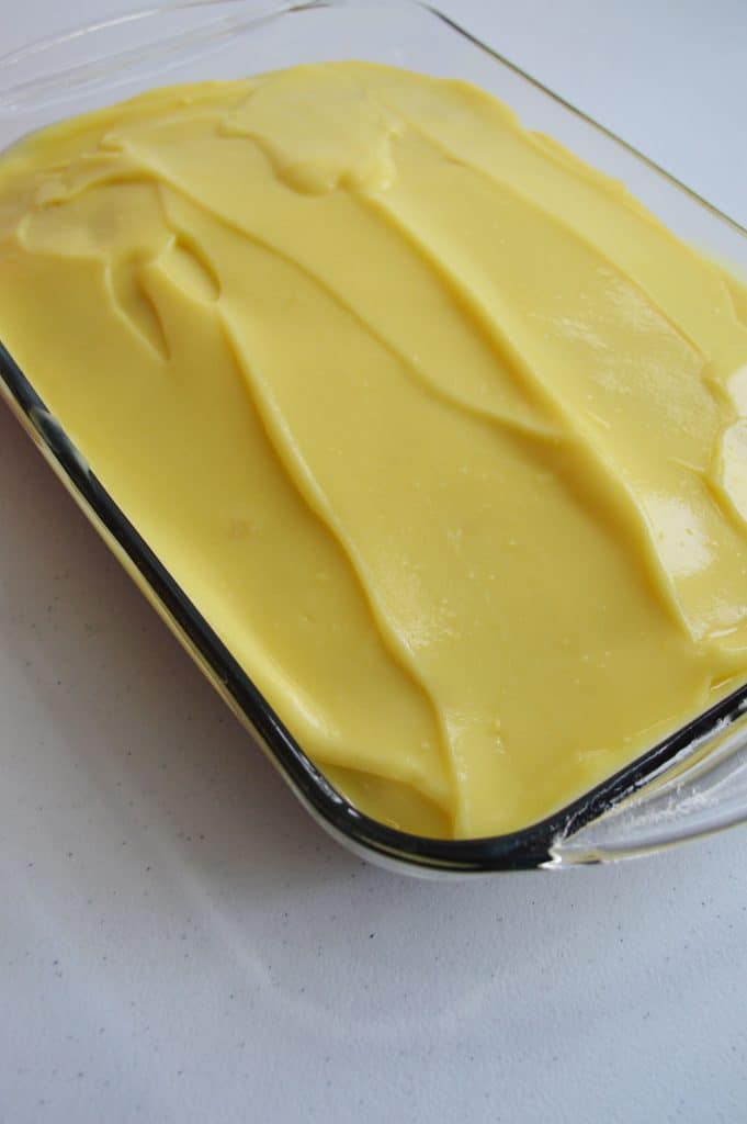 A glass baking dish filled with a smooth, thick layer of creamy yellow custard, spread evenly over the surface—just like the luscious filling in a boston cream poke cake.