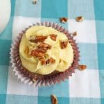 A frosted cupcake topped with chopped pecans on a blue and white checkered cloth.