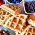 Close-up of golden waffles next to blueberries, chocolate chips, and pecans.