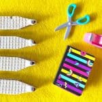 our pencil-shaped wafer cookies, a pair of blue-handled scissors, a pink tape dispenser, and a small striped notebook on a yellow surface.