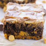Stack of two brownies with swirled tops and chips around on parchment.