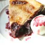 A slice of triple berry pie with a scoop of vanilla ice cream on a plate.