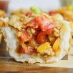 A close-up of Taco Biscuit Cups filled with ground meat, diced red and yellow bell peppers, onions, and melted cheese, sitting on a wooden surface.
