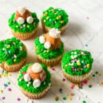 Cupcakes decorated with green frosting, sprinkles, and donut holes to look like bunny tails.