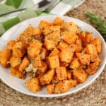 A plate of roasted rosemary sweet potatoes with cheese on top.