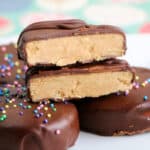 Copycat Reese’s Peanut Butter Eggs, with one cut in half to reveal the creamy peanut butter filling. Some eggs are topped with colorful round sprinkles, set against a brightly patterned background.