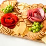 Charcuterie board with crackers, cheese, grapes, and salami and ham arranged like roses.