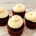 Side view of four frosted chocolate cupcakes in red wrappers.
