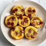 A white plate with eight mini deep dish pizzas topped with melted cheese and pepperoni.