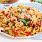 Side view of bruschetta pasta salad on a pink plate with cheese on top.