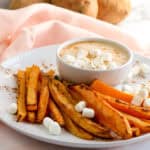 A white plate with baked sweet potato fries, mini marshmallows, and a small bowl of creamy dipping sauce, garnished with marshmallows, makes for delightful fall appetizers on a light pink tablecloth.