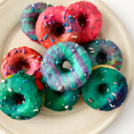 Overhead view of a plate of unicorn donuts with colorful glaze and sprinkles.