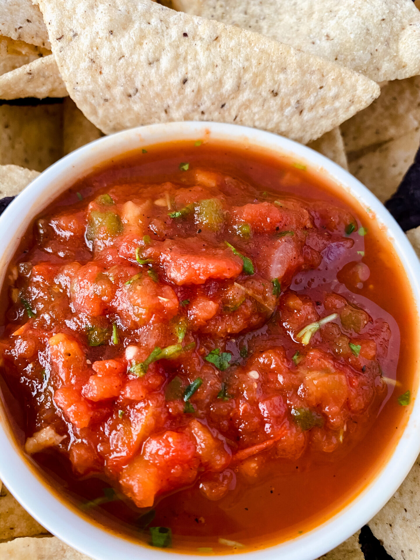 A close-up of a bowl of chunky red salsa with pieces of tomato and herbs, surrounded by tortilla chips—one of the perfect red food recipes for Valentines Day.