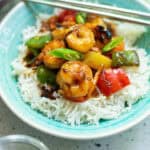 A bowl of white rice topped with shrimp stir-fried with green and red bell peppers and onions, garnished with sliced scallions—one of the perfect dinner ideas for summer nights, served with metal chopsticks resting on the bowl.