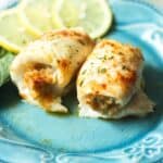 Two pieces of stuffed flounder with crabmeat, rolled and garnished with herbs and paprika, are served on a blue plate with lemon slices and a green leaf in the background.
