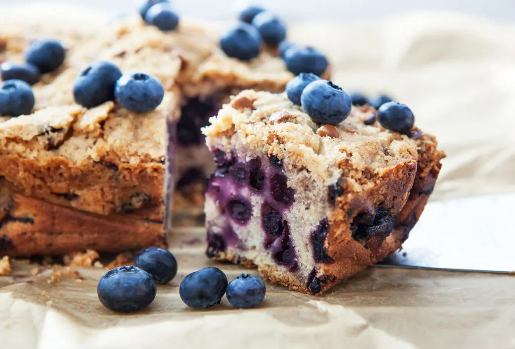 Piece of homemade blueberry cake with berries around, close up