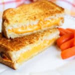 Grilled cheese sandwich halves stacked with melted cheese showing, next to baby carrots.