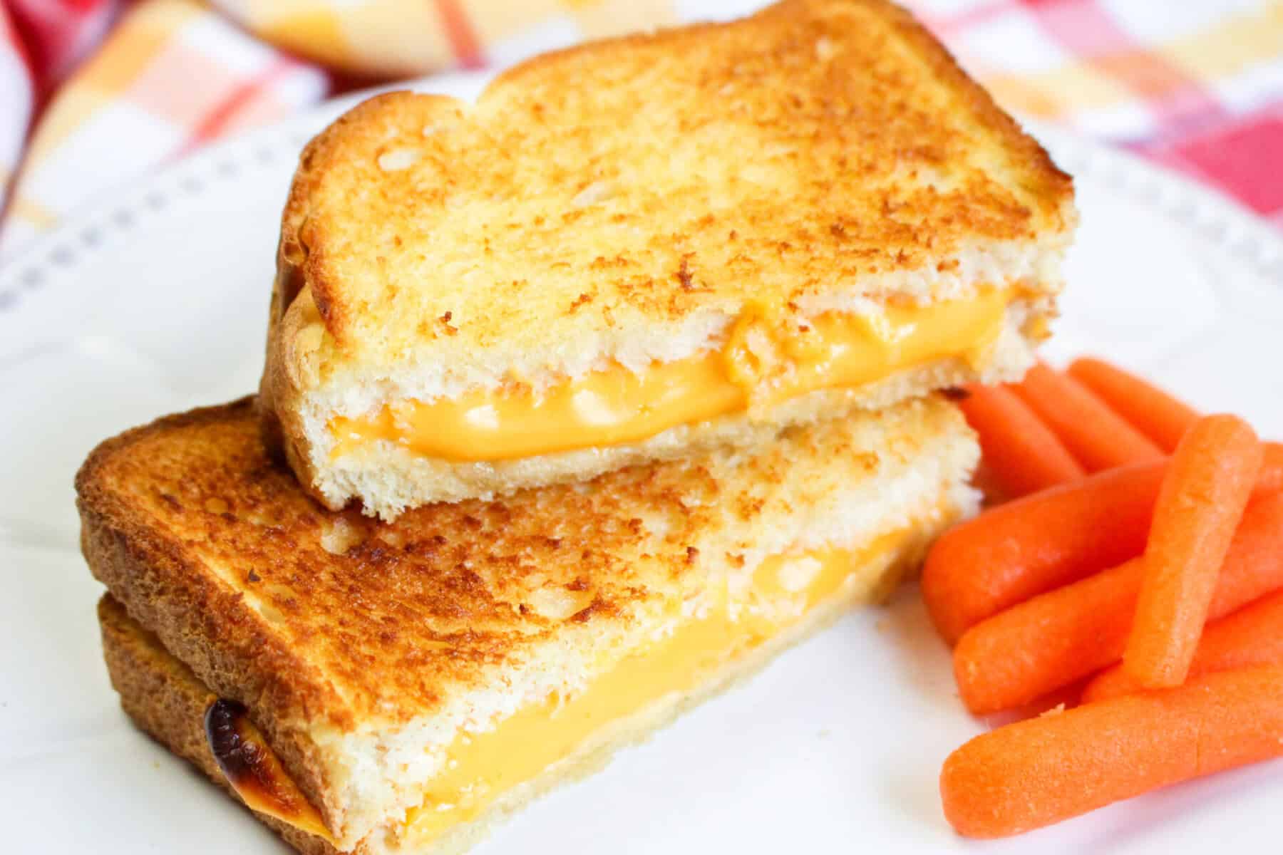 Grilled cheese sandwich halves stacked with melted cheese showing, next to baby carrots.