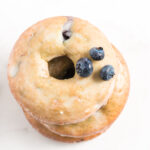 Overhead view of stacked blueberry donuts with three blueberries on top and more scattered nearby.