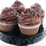Four chocolate cupcakes with chocolate frosting on a black stand.