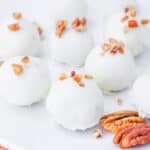 A carrot cake truffle coated in white chocolate and topped with chopped pecans.
