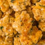 A close-up of a plate filled with golden-brown, cheesy chicken fritters with herbs, stacked and overlapping on a white dish—perfect easy appetizers for a party.