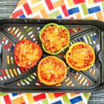 Cooked stuffed peppers in an air fryer basket with melted cheese on top, set over a colorful oven mitt.