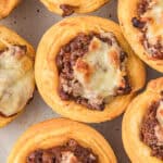 Golden biscuit cups filled with seasoned ground beef and gooey melted cheese, these sloppy joe biscuit cups are arranged closely together on a light-colored plate for a delicious twist on a classic favorite.