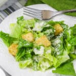 A plate of Caesar salad with romaine lettuce, croutons, grated cheese, and creamy dressing.