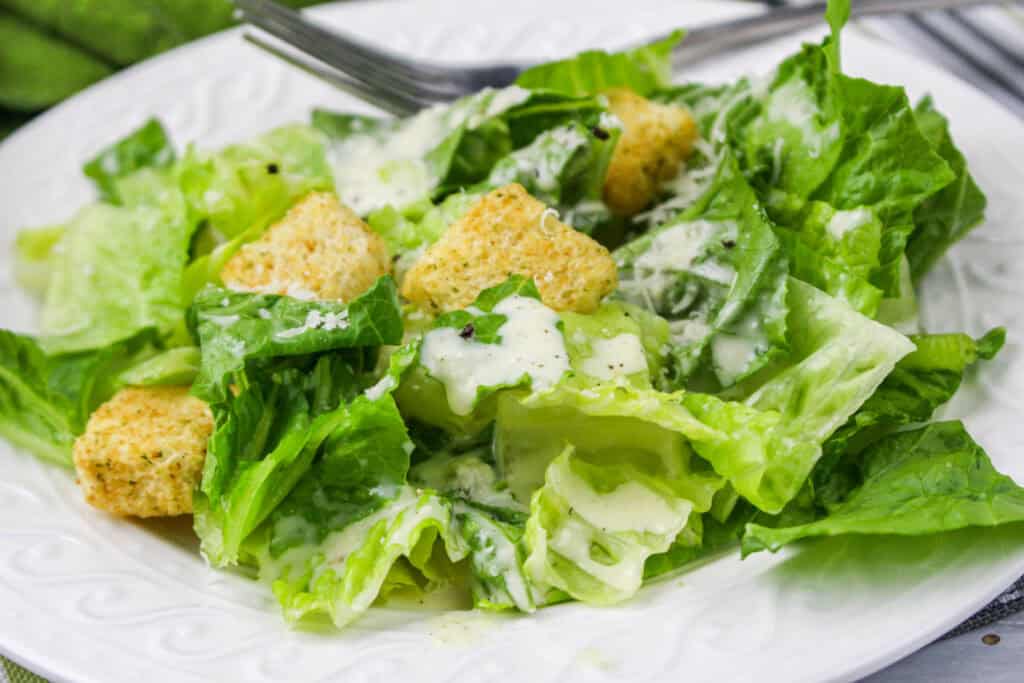 A plate of Caesar salad with romaine lettuce, croutons, grated cheese, and creamy dressing.
