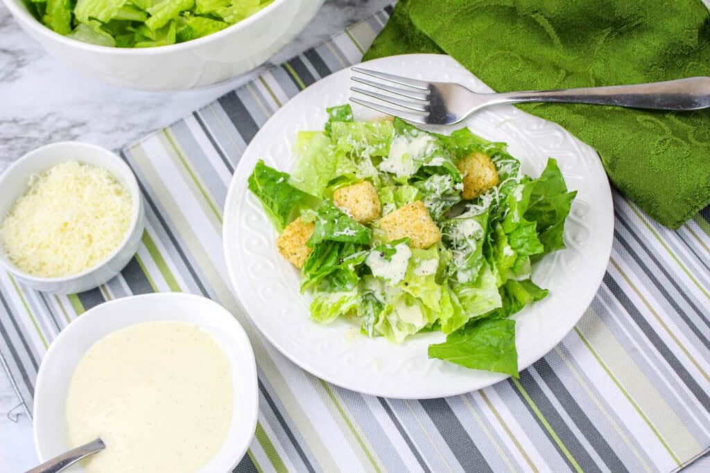 A plate of Caesar salad with romaine lettuce, croutons, grated cheese, and creamy dressing.