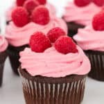 Chocolate cupcakes with pink frosting and three raspberries on top.