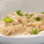 A close-up of creamy shredded Easy Slow Cooker Chicken and Gravy served over mashed potatoes, garnished with fresh parsley in a white bowl.