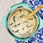 A creamy instant pot chicken gnocchi soup with spinach and carrots is shown in an open teal Instant Pot with a wooden spoon. A blue and white patterned cloth is partially visible beside the pot.