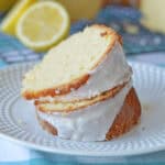 Two slices of glazed lemon pound cake stacked on a plate with lemon halves in the background.