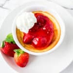 A mini cheesecake topped with strawberry sauce and whipped cream. Two fresh strawberries on the side.