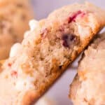 A close-up of a thick cookie with a bite taken out, revealing a soft, moist interior filled with white chocolate chips and bits of red berry, resting on a cooling rack—perfect inspiration for easy cookie recipes.