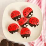 Plate of Oreo cookies decorated as ladybugs with red candy coating, candy eyes, and black icing.