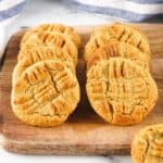 Rows of golden-brown peanut butter cookies with crisscross fork marks are arranged on a wooden cutting board, showcasing a delicious take on classic air fryer desserts, with a striped cloth in the background.