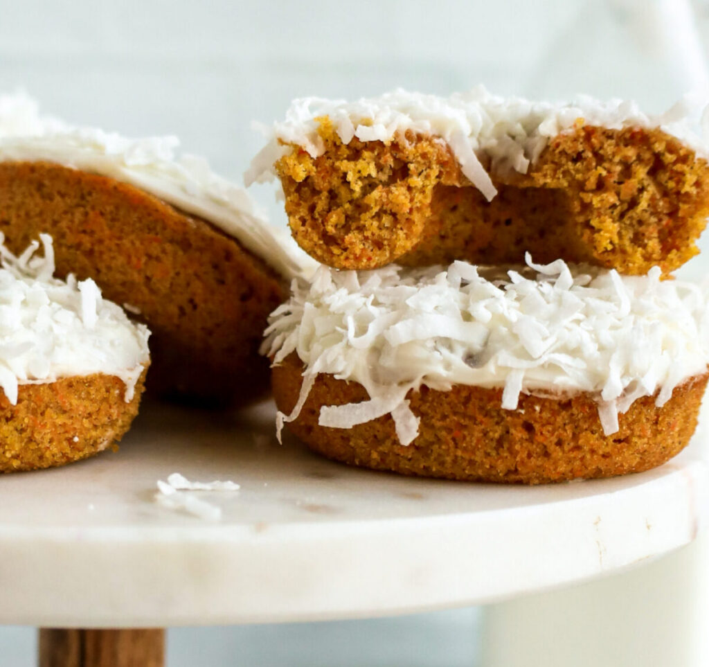 Half of a baked donut topped with white frosting and shredded coconut on a marble cake stand.