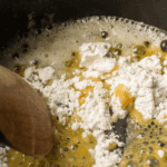 Flour and melted butter are being mixed together in a pan with a wooden spoon, starting to form a classic roux recipe.