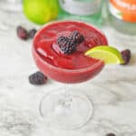 A blackberry daiquiri in a cocktail glass, garnished with fresh blackberries and a lime wedge.