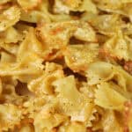 Close-up of air fryer pasta chips made from cooked bow tie pasta (farfalle), coated with light seasoning and melted cheese, showing golden, crispy edges and a slightly glossy texture.
