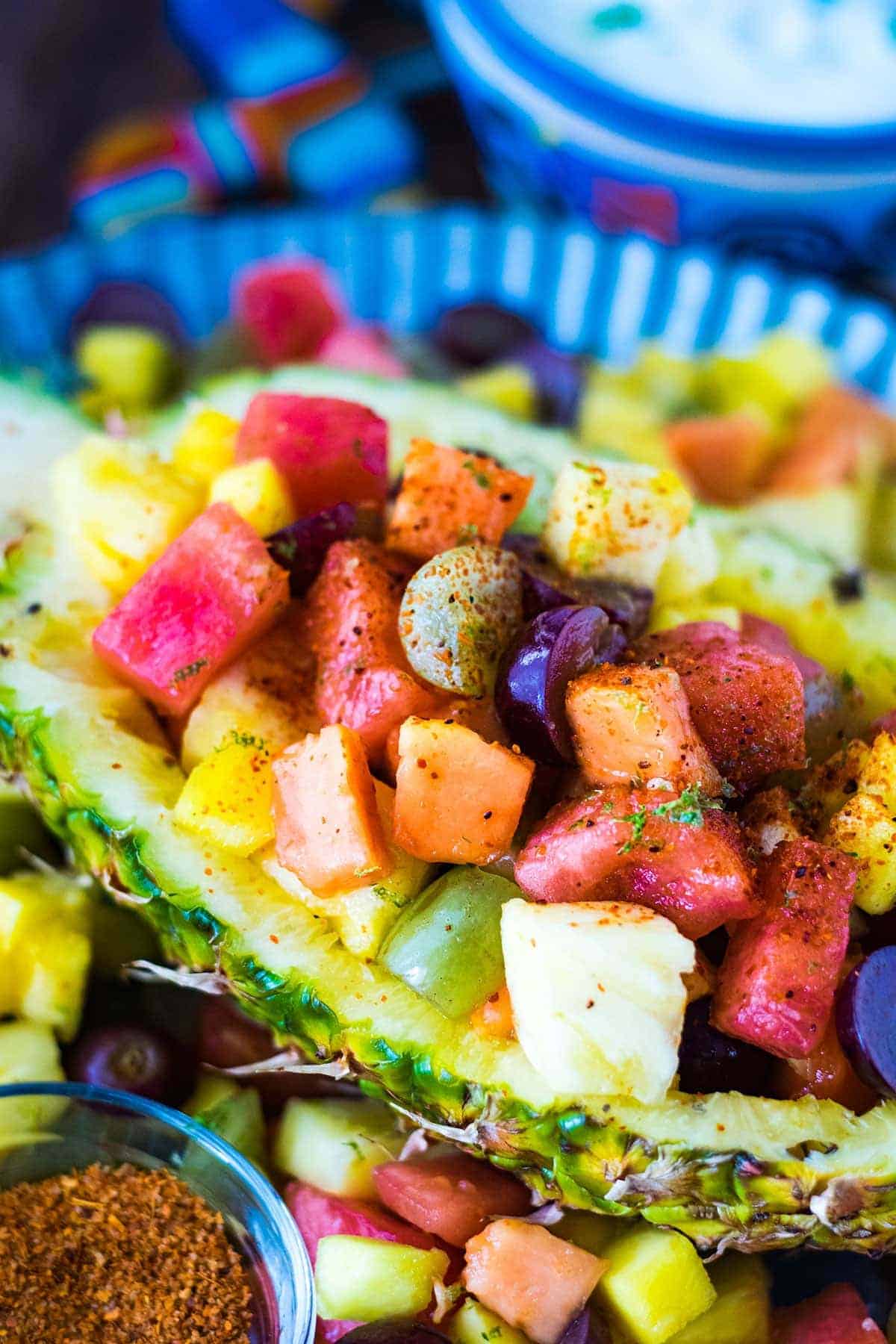 A colorful fruit salad with watermelon, pineapple, grapes, and papaya served in a hollowed-out pineapple half and sprinkled with chili powder—a refreshing twist inspired by Mexican food recipes.