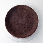 A glass pie dish filled with a pressed mint Oreo pie crust, ready for filling, on a white background.