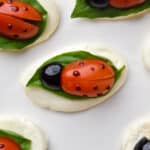Sliced mozzarella topped with basil leaves, grape tomatoes carved to resemble ladybugs, and black olive pieces for heads—these cute bites make delightful finger food ideas for any gathering.